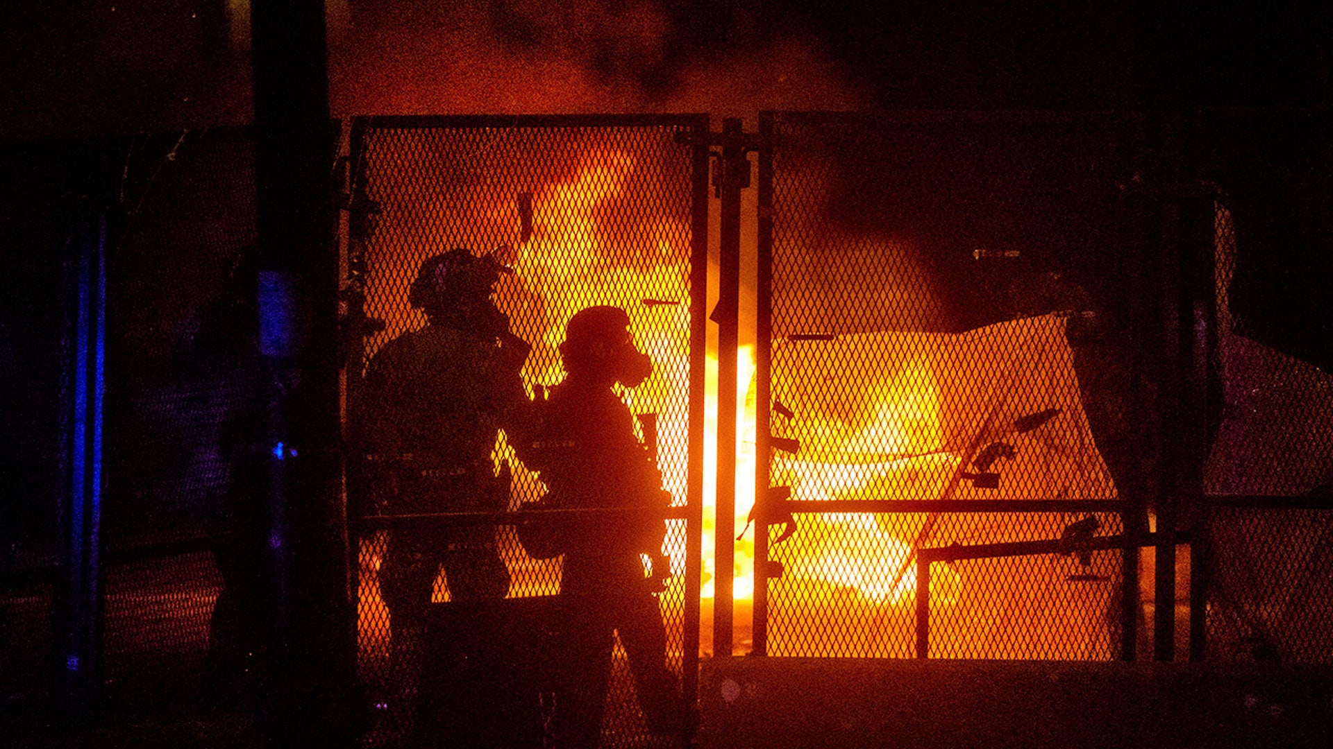 Federal officers guard the Mark O. Hatfield U.S. Courthouse as a fire lit by protesters burns on the other side of a perimeter fence Saturday, July 25, 2020, in Portland, Ore.