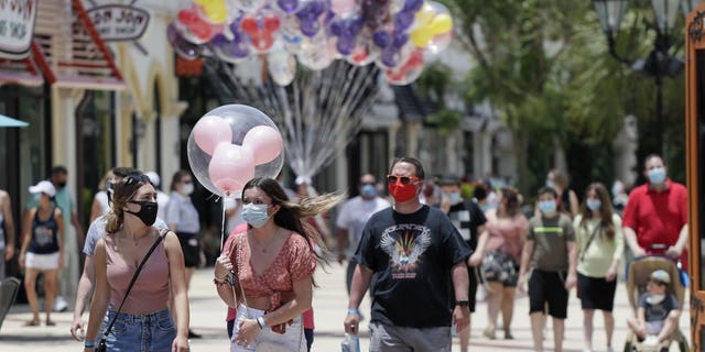 In this June 16, 2020, file photo, guests required to wear masks because of the coronavirus stroll through the Disney Springs shopping, dining and entertainment complex in Lake Buena Vista, Fla. Magic Kingdom and Animal Kingdom will reopen on July 11. In May, the company opened Disney Springs.