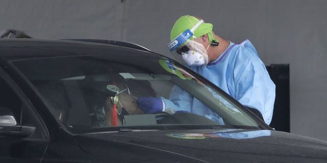 A healthcare worker takes a swab sample from a driver at a drive-through COVID-19 testing site outside Hard Rock Stadium, Wednesday, July 8, 2020, in Miami Gardens, Fla. Florida is one of the nation's hot spots for coronavirus.