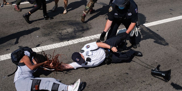 A Black Lives Matter protester and NYPD officers scuffle on the Brooklyn Bridge during a demonstration, Wednesday, July 15, 2020, in New York. (AP Photo/Yuki Iwamura)