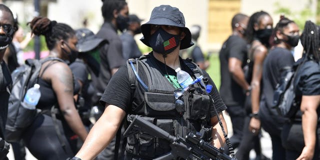 An armed member of the "NFAC" scans the crowd during a march through downtown toward the Hall of Justice in Louisville, Ky., Saturday, July 25, 2020. Hundreds of activists demanded justice for Breonna Taylor during the demonstrations in her hometown that drew counter-protesters from a white militia group. Taylor, a 26-year-old EMT, was fatally shot when police officers burst into her Louisville apartment using a no-knock warrant during an investigation.(AP Photo/Timothy D. Easley)