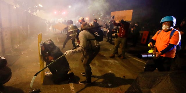 Demonstrators shield themselves from tear gas launched over a fence by federal officers during a Black Lives Matter protest at the Mark O. Hatfield United States Courthouse Friday, July 24, 2020, in Portland, Ore. 