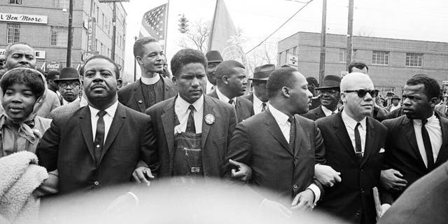 In this March 17, 1965, file photo, Dr. Martin Luther King Jr., fourth from left, foreground, locks arms with his aides as he leads a march of several thousands to the courthouse in Montgomery, Ala. From left are: an unidentified woman, Rev. Ralph Abernathy, James Foreman, King, Jesse Douglas Sr., and John Lewis. (AP Photo/File)