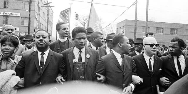 In this March 17, 1965, file photo, Dr. Martin Luther King Jr., fourth from left, foreground, locks arms with his aides as he leads a march of several thousands to the courthouse in Montgomery, Ala. From left are: an unidentified woman, Rev. Ralph Abernathy, James Foreman, King, Jesse Douglas Sr., and John Lewis. (AP Photo/File)