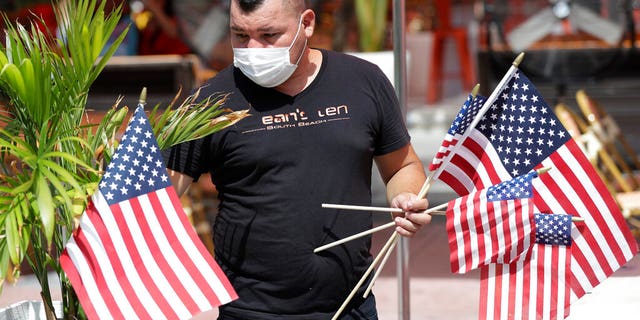 Marvin Turcios puts out American flags at Ocean's 10 restaurant on Miami Beach, Florida's famed Ocean Drive on South Beach, July 4, 2020. The Fourth of July holiday weekend began Saturday with some sobering numbers in the Sunshine State: Florida logged a record number of people testing positive for the coronavirus. 