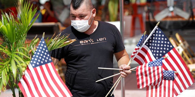 Marvin Turcios puts out American flags at Ocean's 10 restaurant on Miami Beach, Florida's famed Ocean Drive on South Beach, July 4, 2020. The Fourth of July holiday weekend began Saturday with some sobering numbers in the Sunshine State: Florida logged a record number of people testing positive for the coronavirus.
