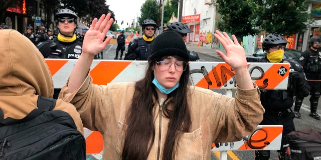 A protester stands with her hand up in front of a road blocked by Seattle police in the Capitol Hill Organized Protest zone early Wednesday. Police in Seattle have torn down demonstrators' tents in the city's so-called occupied protest zone after the mayor ordered it cleared. (AP Photo/Aron Ranen)