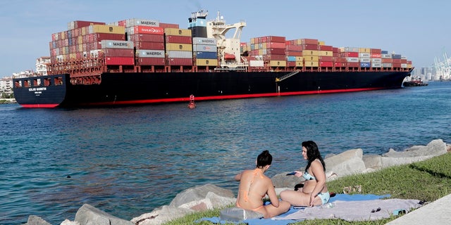 Women sunbathe on a strip of grass along Government Cut as a container ship passes by during the new coronavirus pandemic, Friday in Miami Beach, Fla. Beaches throughout South Florida are closed for the busy Fourth of July weekend to avoid further spread of the new coronavirus. (AP Photo/Lynne Sladky)