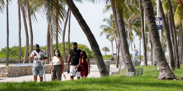 A group of people, wearing face masks to prevent the spread of the coronavirus, walk along a beach path on Miami Beach, Florida's famed South Beach, July 4, 2020. 