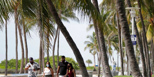 A group of people, wearing face masks to prevent the spread of the coronavirus, walk along a beach path on Miami Beach, Florida's famed South Beach, July 4, 2020.
