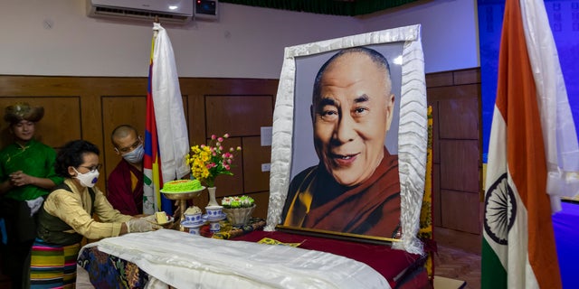 An exile Tibetan offers a piece of cake to a portrait of her spiritual leader the Dalai Lama to mark her leader's 85th birthday in Dharmsala, India, Monday, July 6, 2020. (AP Photo/Ashwini Bhatia)