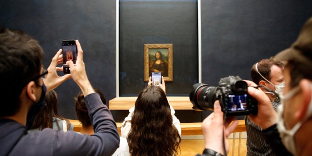 Visitors take photos of the Leonardo da Vinci's painting Mona Lisa, in Paris, Monday, July 6, 2020. The home of the world's most famous portrait, the Louvre Museum in Paris, reopened Monday after a four-month coronavirus lockdown. (AP Photo/ Thibault Camus)