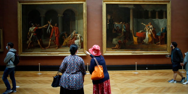 Visitors watch oil on canvas entitled Le serment des Horaces, left, and Licteurs rapportant à Brutus le corps de ses fils, by Jacques Louis David in the Louvre Museum, in Paris, Monday, July 6, 2020. The home of the world's most famous portrait, the Louvre Museum in Paris, reopened Monday after a four-month coronavirus lockdown. (AP Photo/ Thibault Camus)