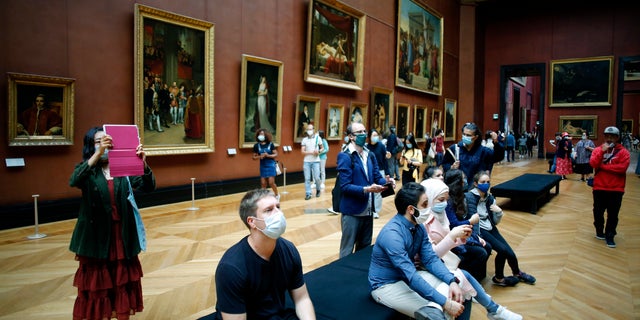Visitors watch oil on canvas of 1807 entitled Le Sacre de Napoleon by Jacques Louis David, at the Louvre Museum, in Paris, Monday, July 6, 2020. The home of the world's most famous portrait, the Louvre Museum in Paris, reopened Monday after a four-month coronavirus lockdown. (AP Photo/ Thibault Camus)