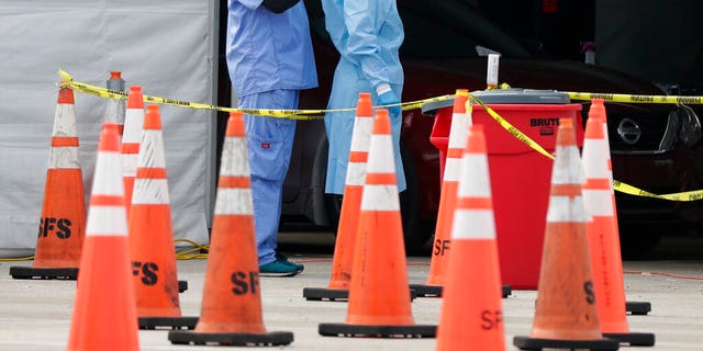 In this July 5, 2020, file photo, healthcare workers help each other with their personal protective equipment at a drive-thru coronavirus testing site outside Hard Rock Stadium in Miami Gardens, Fla.