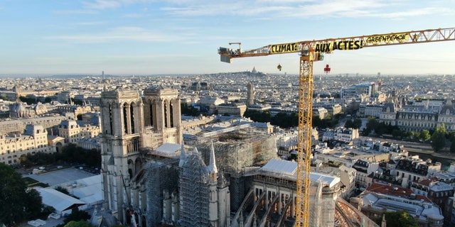 In this handout photograph provided by Greenpeace, a banner hanging from a crane reads "Climate. In action", near Notre Dame Cathedral, in Paris, Thursday, July 9, 2020. Greenpeace activists hung banners from the huge construction crane atop Notre Dame Cathedral in Paris on Thursday accusing France and President Emmanuel Macron of not doing enough to fight climate change. (AP Photo/Greenpeace, HO)