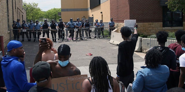 A protester holds a newspaper in front of the Minneapolis police standing guard against protesters at the Third Precinct as people protest the arrest and death of George Floyd on May 27, 2020. (AP Photo/Jim Mone, File)