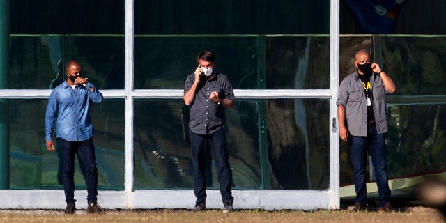 Brazil's President Jair Bolsonaro, center, talks on his phone while standing outside his official residence Alvorada Palace, in Brasilia, Brazil, Friday, July 10, 2020. (AP Photo/Eraldo Peres)