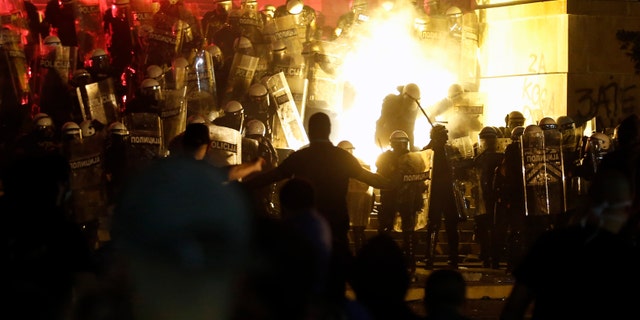 Protesters clash with riot police on the steps of the Serbian parliament during a protest in Belgrade, Serbia, Friday, July 10 2020. Hundreds of demonstrators tried to storm Serbia's parliament on Friday, clashing with police who fired tear gas during the fourth night of protests against the president's increasingly authoritarian rule. (AP Photo/Darko Vojinovic)