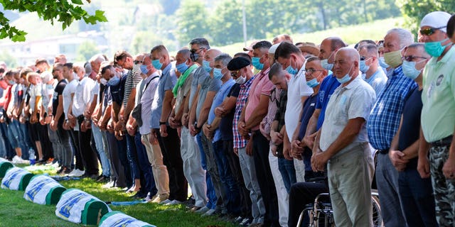 Bosnian pray by the coffins of the victims during the burrial in Potocari, near Srebrenica, Bosnia, Saturday, July 11, 2020. 