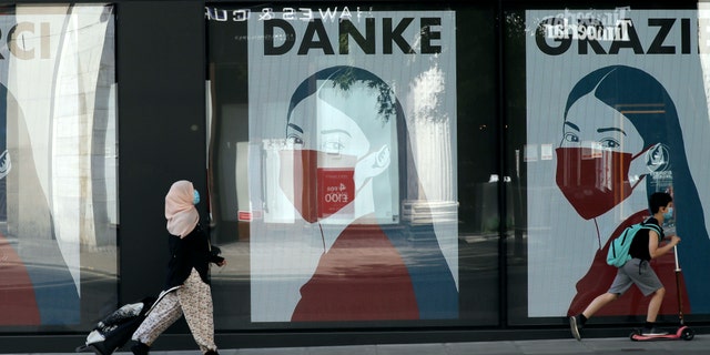 A woman and child wearing face masks past a coronavirus related artwork displayed on screens in the window of the Flannels clothing store on Oxford Street, in central London, Thursday, May 21, 2020. (AP Photo/Matt Dunham)