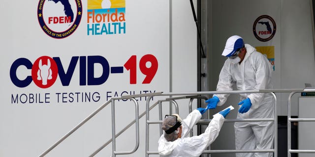 Health care workers work at a walk-up COVID-19 testing site during the coronavirus pandemic, Friday, July 17, 2020, in Miami Beach, Fla. People getting tested are separated from nurses via a glass pane.