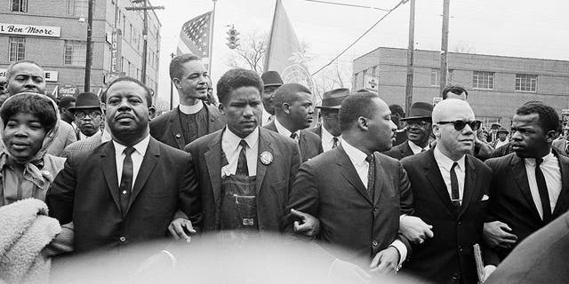 In this March 17, 1965, file photo, Dr. Martin Luther King Jr., fourth from left, foreground, locks arms with his aides as he leads a march of several thousands to the courthouse in Montgomery, Ala. From left are: an unidentified woman, Rev. Ralph Abernathy, James Foreman, King, Jesse Douglas Sr., and John Lewis. 
