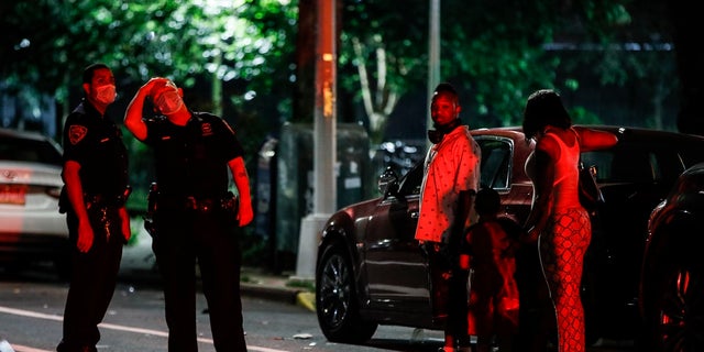 Police officers speak to locals at a crime scene on Atlantic Avenue where two individuals were injured by gunfire on July 18 in Brooklyn. Police statistics show more people have been shooting victims this year than all of last year. (AP Photo/John Minchillo)