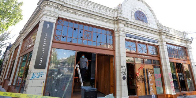 A worker clears glass from broken windows at the Starbucks Roastery, Sunday, July 19, 2020 in Seattle's Capitol Hill neighborhood. Protesters broke windows at the store earlier in the afternoon. (AP Photo/Ted S. Warren)