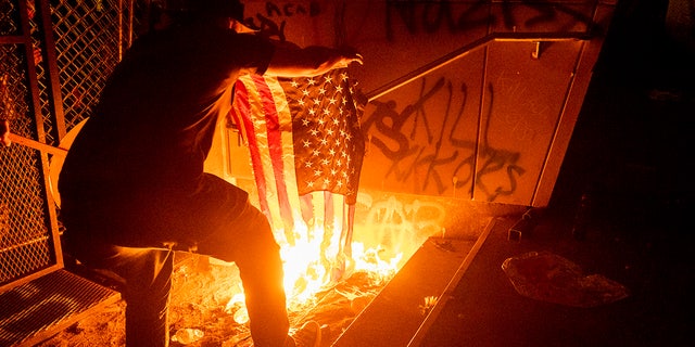 A Black Lives Matter protester burns an American flag outside the Mark O. Hatfield United States Courthouse on Monday, July 20, 2020, in Portland, Ore.  (AP Photo/Noah Berger)