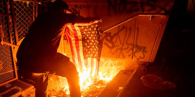 A Black Lives Matter protester burns an American flag outside the Mark O. Hatfield United States Courthouse on Monday, July 20, 2020, in Portland, Ore.  (AP Photo/Noah Berger)