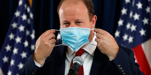 Colorado Governor Jared Polis puts on his face mask after concluding a news conference on the state's efforts against the new coronavirus Tuesday, July 21, 2020, in Denver. (AP Photo/David Zalubowski)