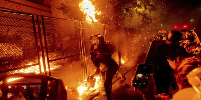 Protesters throw flaming debris over a fence at the Mark O. Hatfield United States Courthouse on July 22, in Portland, Ore. Following a larger Black Lives Matter Rally, several hundred demonstrators faced off against federal officers at the courthouse. (AP Photo/Noah Berger)