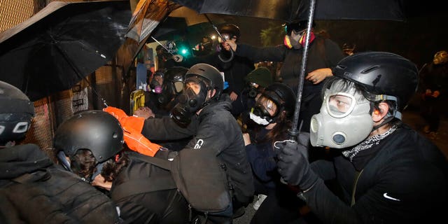 Demonstrators shield themselves from tear gas launched over a fence by federal officers during a Black Lives Matter protest at the Mark O. Hatfield United States Courthouse Friday, July 24, 2020, in Portland, Ore. 