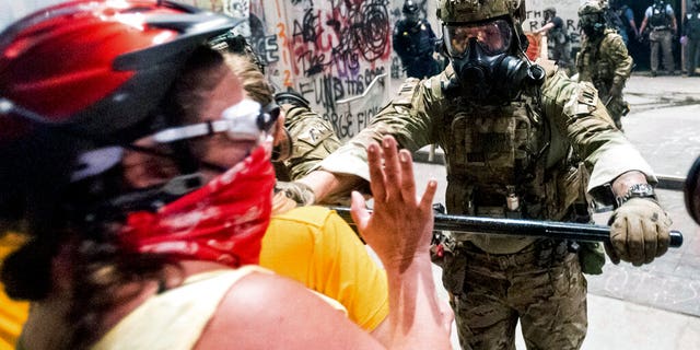 In this July 21, 2020 file photo, a federal officer pushes back demonstrators at the Mark O. Hatfield United States Courthouse in Portland, Ore. (AP Photo/Noah Berger, File)