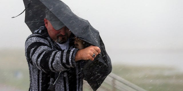 A man holds the front on his umbrella as he fights heavy rain and wind on Seawall Boulevard in Galveston, Texas, Saturday, July 25, 2020. (Associated Press)