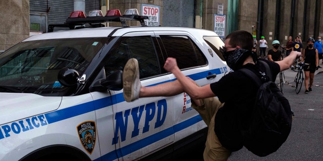 A protester kicks a police vehicle in an attempt to break its side mirror during a "Solidarity with Portland" protest Saturday, July 25, 2020, in New York. (AP Photo/Yuki Iwamura)