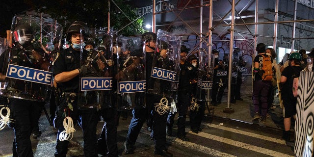 New York Police Department officers walk down a street with shields during a 