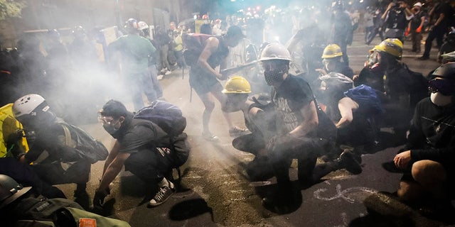 Demonstrators sit and kneel as tear gas fills the air during a Black Lives Matter protest at the Mark O. Hatfield United States Courthouse Sunday, July 26, 2020, in Portland, Ore. (AP Photo/Marcio Jose Sanchez)