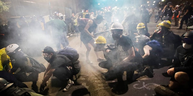 Demonstrators sit and kneel as tear gas fills the air during a Black Lives Matter protest at the Mark O. Hatfield United States Courthouse Sunday, July 26, 2020, in Portland, Ore. (AP Photo/Marcio Jose Sanchez)