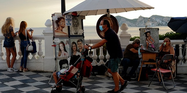 A tourist pushes a stroller as illustrators wait for customers, in Benidorm, south-east Spain, Monday, July 27, 2020.  (AP Photo/Alvaro Barrientos)