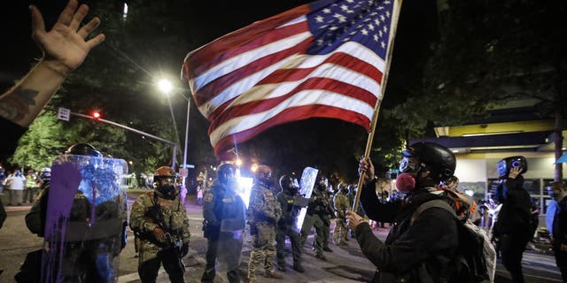 election 2020 Donald Trump President Trump Conservative News RNC A demonstrator waves a U.S. flag in front of federal officers after tear gas is deployed during a Black Lives Matter protest at the Mark O. Hatfield United States Courthouse July 30, in Portland, Ore. (AP Photo/Marcio Jose Sanchez)
