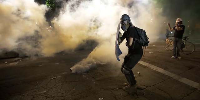 A demonstrator tries to shield himself from tear gas deployed by federal agents during a Black Lives Matter protest at the Mark O. Hatfield United States Courthouse Wednesday, July 29, 2020, in Portland, Ore. (AP Photo/Marcio Jose Sanchez)