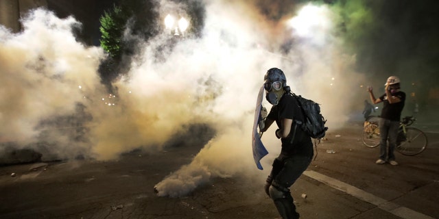 A demonstrator tries to shield himself from tear gas deployed by federal agents during a Black Lives Matter protest at the Mark O. Hatfield United States Courthouse Wednesday, July 29, 2020, in Portland, Ore. (AP Photo/Marcio Jose Sanchez)