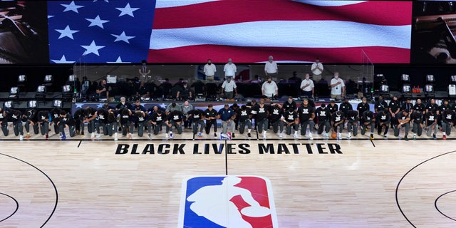 Members of the New Orleans Pelicans and Utah Jazz kneel together around the Black Lives Matter logo on the court during the national anthem before the start of an NBA basketball game Thursday, July 30, 2020, in Lake Buena Vista, Fla. (AP Photo/Ashley Landis, Pool)