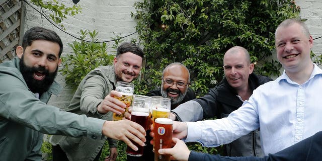 Men enjoy their first beers as the Chandos Arms pub reopens, in London, Saturday, July 4, 2020. England is embarking on perhaps its biggest lockdown easing yet as pubs and restaurants have the right to reopen for the first time in more than three months. In addition to the reopening of much of the hospitality sector, couples can tie the knot once again, while many of those who have had enough of their lockdown hair can finally get a trim.