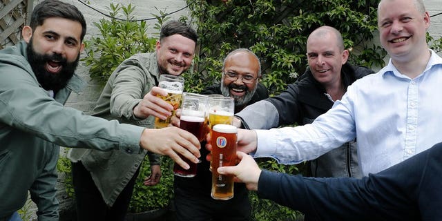 Men enjoy their first beers as the Chandos Arms pub reopens, in London, Saturday, July 4, 2020. England is embarking on perhaps its biggest lockdown easing yet as pubs and restaurants have the right to reopen for the first time in more than three months. In addition to the reopening of much of the hospitality sector, couples can tie the knot once again, while many of those who have had enough of their lockdown hair can finally get a trim.