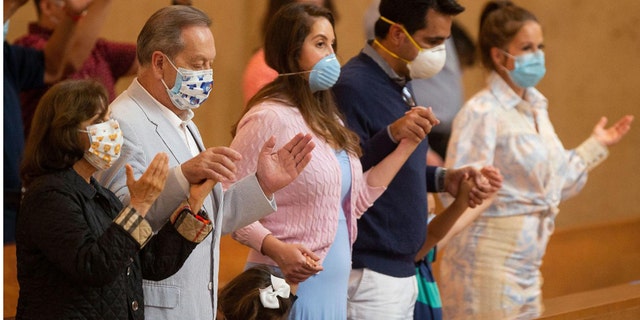 Family members hold hands as they pray at the first English Mass with faithful present at the Cathedral of Our Lady of the Angels in downtown Los Angeles, Sunday, June 7, 2020. Catholic parishes throughout the Archdiocese of Los Angeles suspended public Mass in March amid the coronavirus outbreak. (AP Photo/Damian Dovarganes)