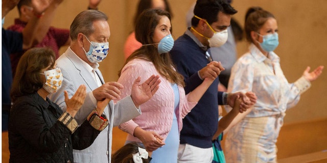 Family members hold hands as they pray at the first English Mass with faithful present at the Cathedral of Our Lady of the Angels in downtown Los Angeles, Sunday, June 7, 2020. Catholic parishes throughout the Archdiocese of Los Angeles suspended public Mass in March amid the coronavirus outbreak. (AP Photo/Damian Dovarganes)