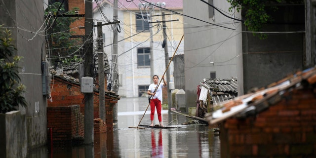 A woman pushes a makeshift raft down a flooded alleyway in a village in Yongxiu in central eastern China's Jiangxi province, Thursday, July 16, 2020.